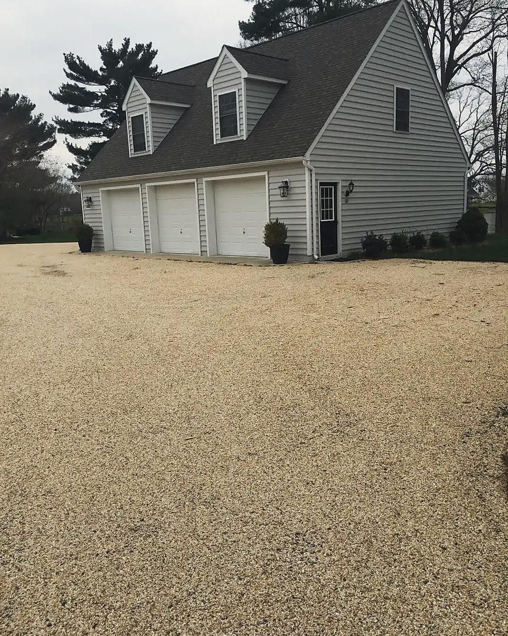 A tan tar and chip drive at a three-car garage