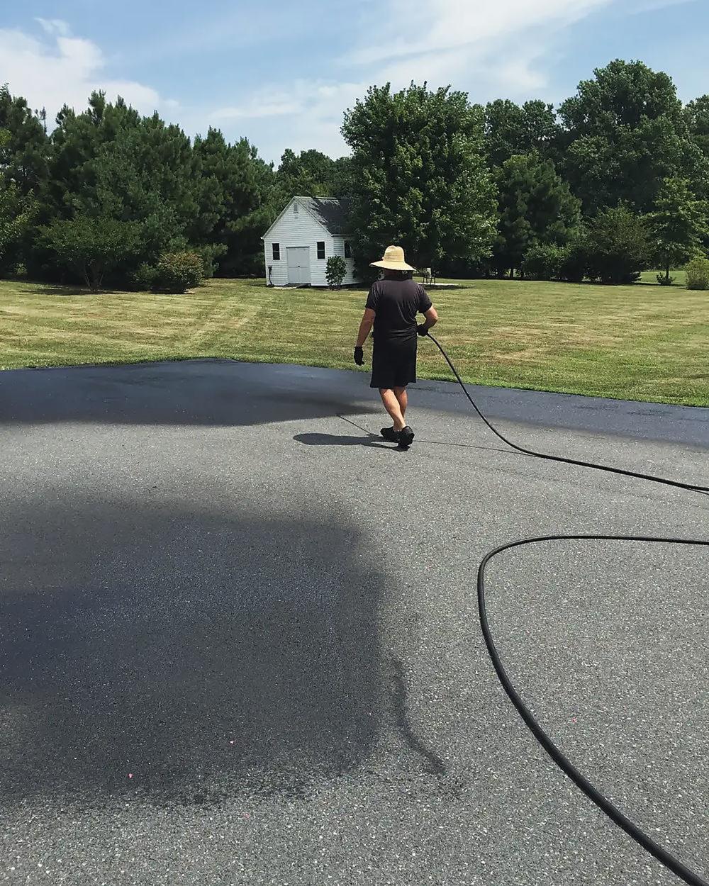 Sealer being sprayed across a wide asphalt drive
